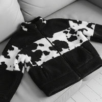 Black and white cow print jacket worn by a person on a light gray background