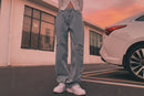 A person standing outdoors wearing light blue straight jeans and white sneakers.