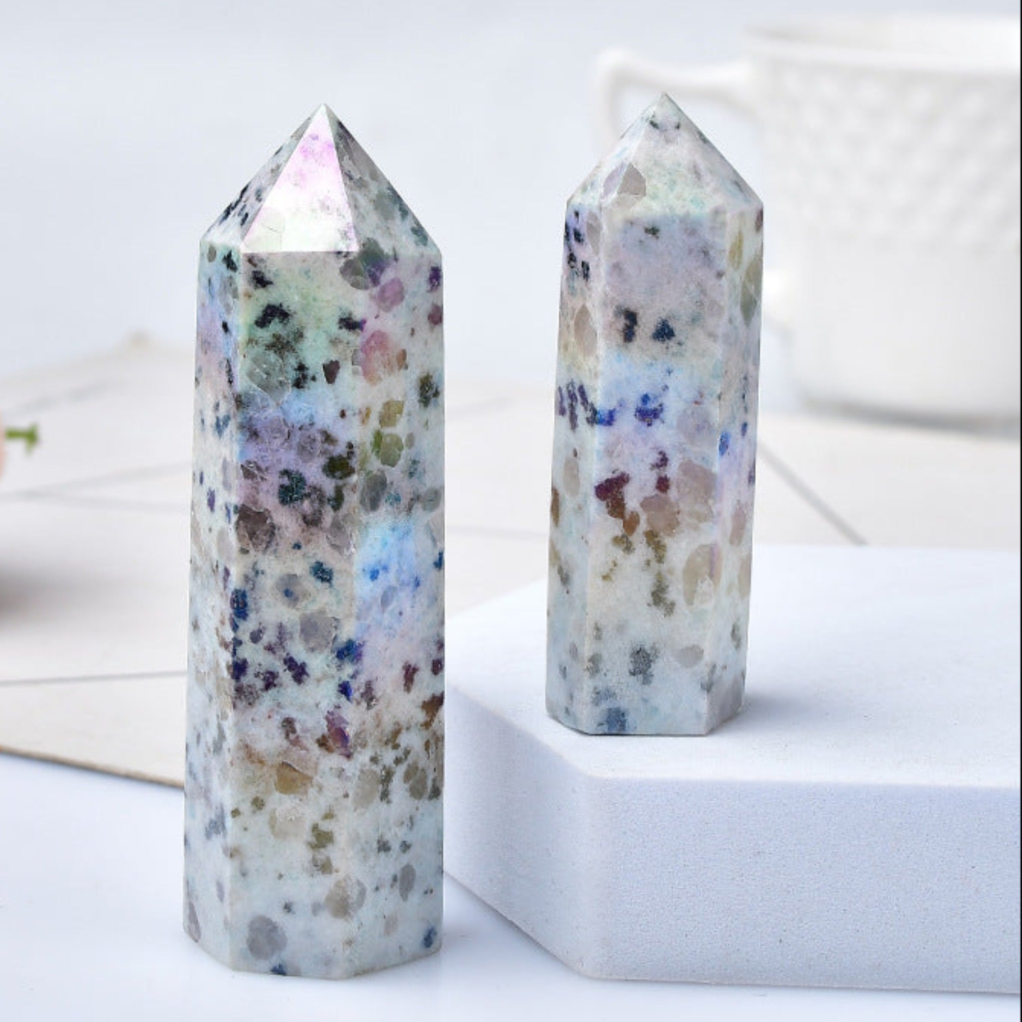 Two natural crystal stones with a blue rough texture, placed on a white surface with a decorative flower and a cup in the background.