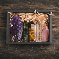 Set of crystals including amethyst, tiger's eye, and rose quartz in a box on a wooden surface