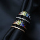 A ring with multiple bands featuring a rainbow chakra design with microdiamond inlays, displayed on a soft fabric surface.