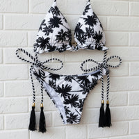Black and white bikini set with palm tree pattern hanging against a white brick wall.