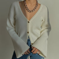 Person wearing a white cardigan over a blue top with a neutral background