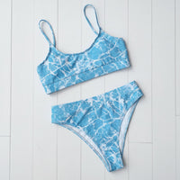 Blue and white marble patterned bikini set on a light wooden floor.