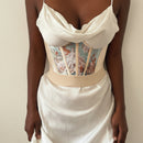 Woman wearing a white satin slip dress with floral corset details on a plain background