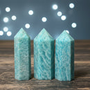 Three turquoise crystal towers on a wooden surface with a blurred light background