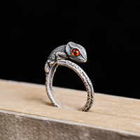 Silver lizard-shaped ring with a red stone on a wooden surface