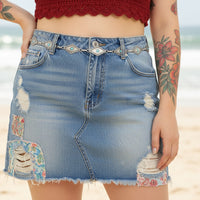 Person wearing a denim skirt with an ornate belt and red top on a beige background