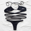 Black bikini set on a white surface with a hat and plant in the background