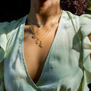 Person wearing a light green blouse with a deep neckline and gold necklaces.