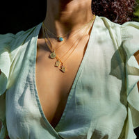 Person wearing a light green blouse with a deep neckline and gold necklaces.
