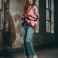 Woman wearing a red and white patterned sweater and blue jeans standing in an abandoned building.