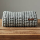 Knitted blanket with a brown label on a wooden surface against a gray background