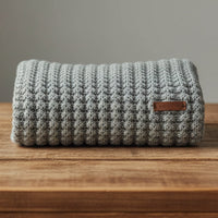 Knitted blanket with a brown label on a wooden surface against a gray background