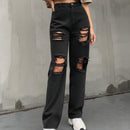 Person wearing a white long-sleeve crop top and black ripped jeans against a gray wall.