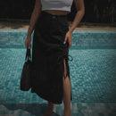Person wearing a black skirt with lace top, standing barefoot by a pool.