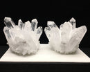 Two crystal formations on a white platform with a black background