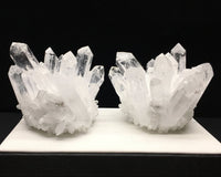 Two crystal formations on a white platform with a black background