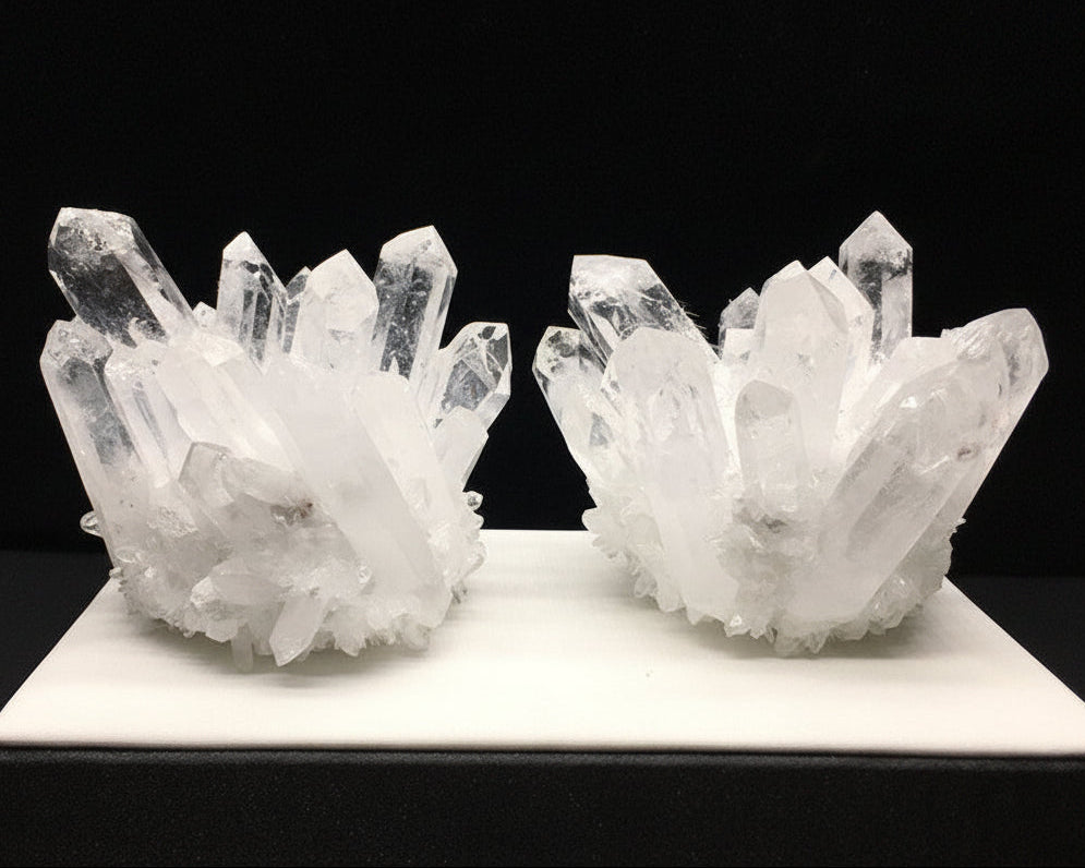 Two crystal formations on a white platform with a black background