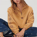 Person wearing a mustard yellow pullover with sun designs on sleeves and chest, sitting on a white background.