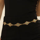Person wearing a black outfit with a decorative gold belt featuring turquoise stones on a beige background
