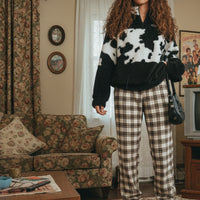Person wearing a cow print sweater and ripped jeans in a room with a couch and window.
