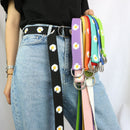 Person wearing a black belt with white daisy pattern holding colorful belts.