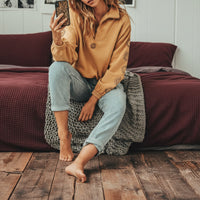 Woman sitting on a leopard print ottoman wearing a mustard yellow sweatshirt and light blue jeans.