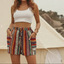 Woman standing in front of a beige tent wearing a white top and colorful shorts.