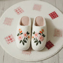 Pair of white slippers with floral embroidery on a soft surface.