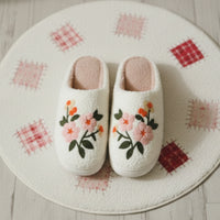 Pair of white slippers with floral embroidery on a soft surface.