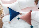 Decorative pillows with pom-poms on a bed with a side table and flowers.