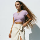 Person wearing a purple crop top and blue jeans against a light background