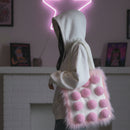 Person wearing a white hoodie with a pink pom-pom bag in a room with a neon sign and framed pictures.