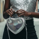 Silver heart-shaped handbag held by a person against a plain background