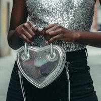Silver heart-shaped handbag held by a person against a plain background