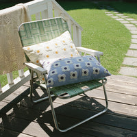 Floral-patterned cushions on a woven stool against a neutral wall.