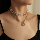 Necklace with pearl accents and a lock charm on a person wearing a black top.