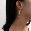 A person wearing a gold-colored cross-shaped earring with a red water drop design, and a matching gold-colored pendant.