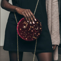 Person holding a red velvet handbag with star and moon designs.