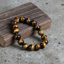 A round natural stone bracelet with a mix of brown and black agate beads, displayed on a wooden surface.