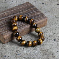A round natural stone bracelet with a mix of brown and black agate beads, displayed on a wooden surface.