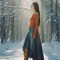 Woman in an orange top and blue skirt standing in a snowy forest