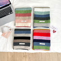 Four striped fabric swatches in various colors on a white surface with a laptop and mug.