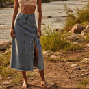 Woman in a lace top and denim skirt standing by a river with greenery in the background