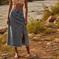Woman in a lace top and denim skirt standing by a river with greenery in the background