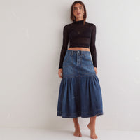 Person wearing a black crop top, blue denim skirt, and black boots against a white background