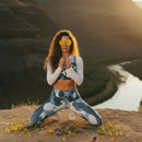 Woman in a patterned outfit holding flowers against a mountainous landscape
