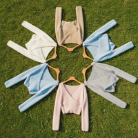 Set of six cropped sweaters in different colors on hangers, laying in a circle on the grass
