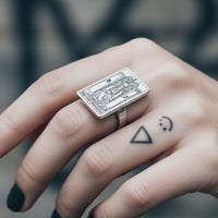 Hand wearing a silver playing card ring with a blurred background